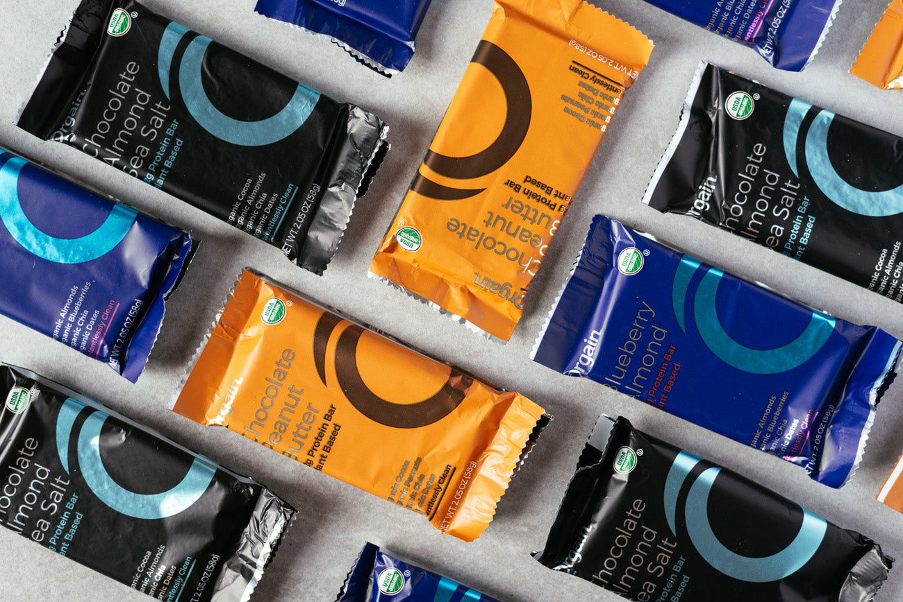 Health bars in colorful packaging labeled with flavors like "chocolate peanut butter" and "blueberry almond" are displayed on a flat surface.