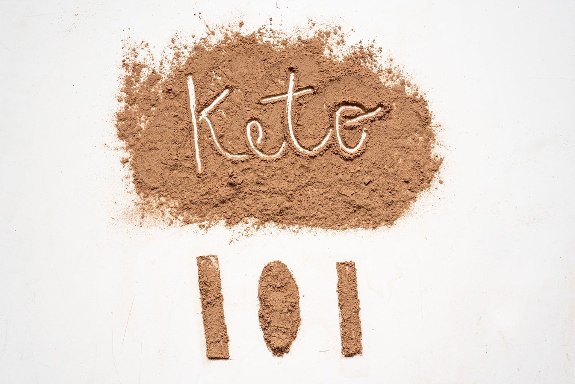 Light brown powder spread on a white surface with "Keto" written in it, and three vertical lines resembling "101" below.