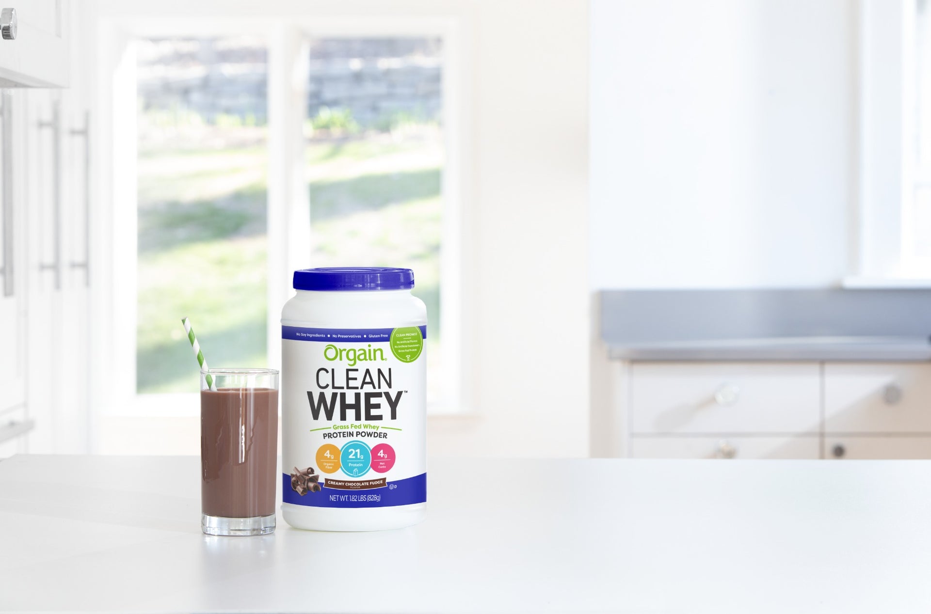 Orgain Clean Whey Protein Powder and a glass of chocolate shake on a white kitchen countertop.