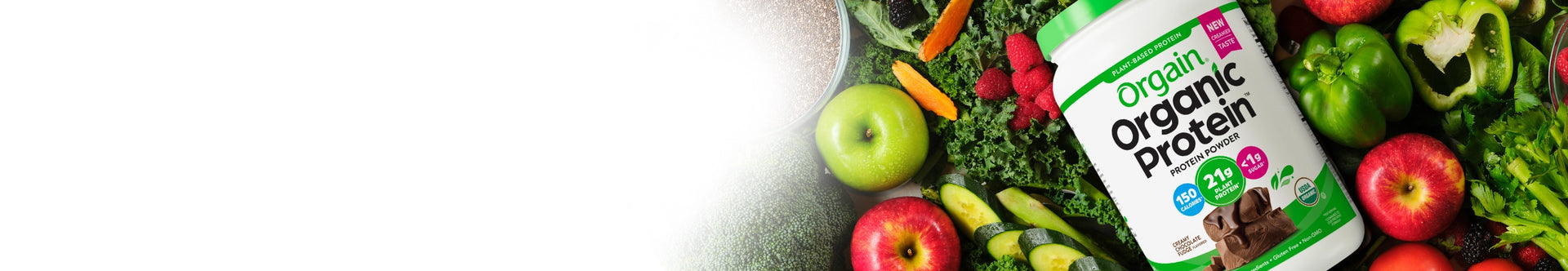 orgain organic protein powder laying on a table of vegetables.