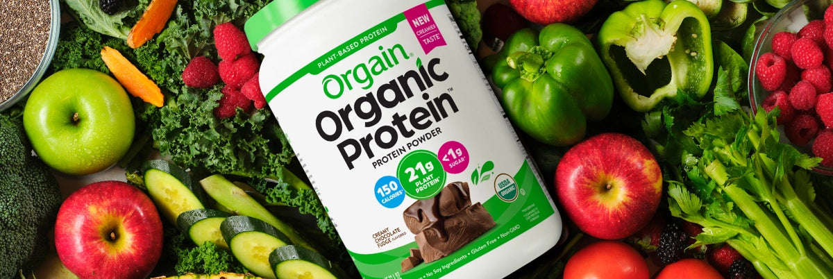 orgain organic protein powder laying on a table of vegetables.