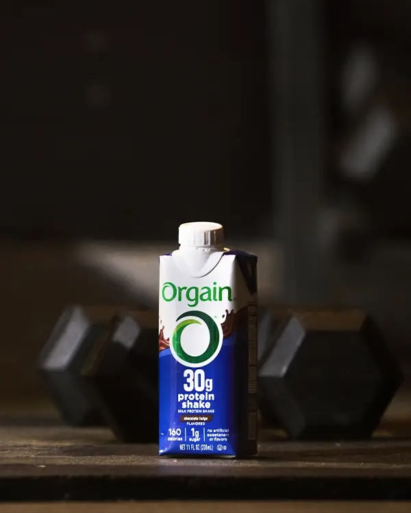 30g protein shake in front of a pair of dumbbells