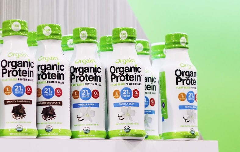 Orgain Organic Protein bottles on a shelf, featuring green caps and flavors like Smooth Chocolate and Vanilla Bean.