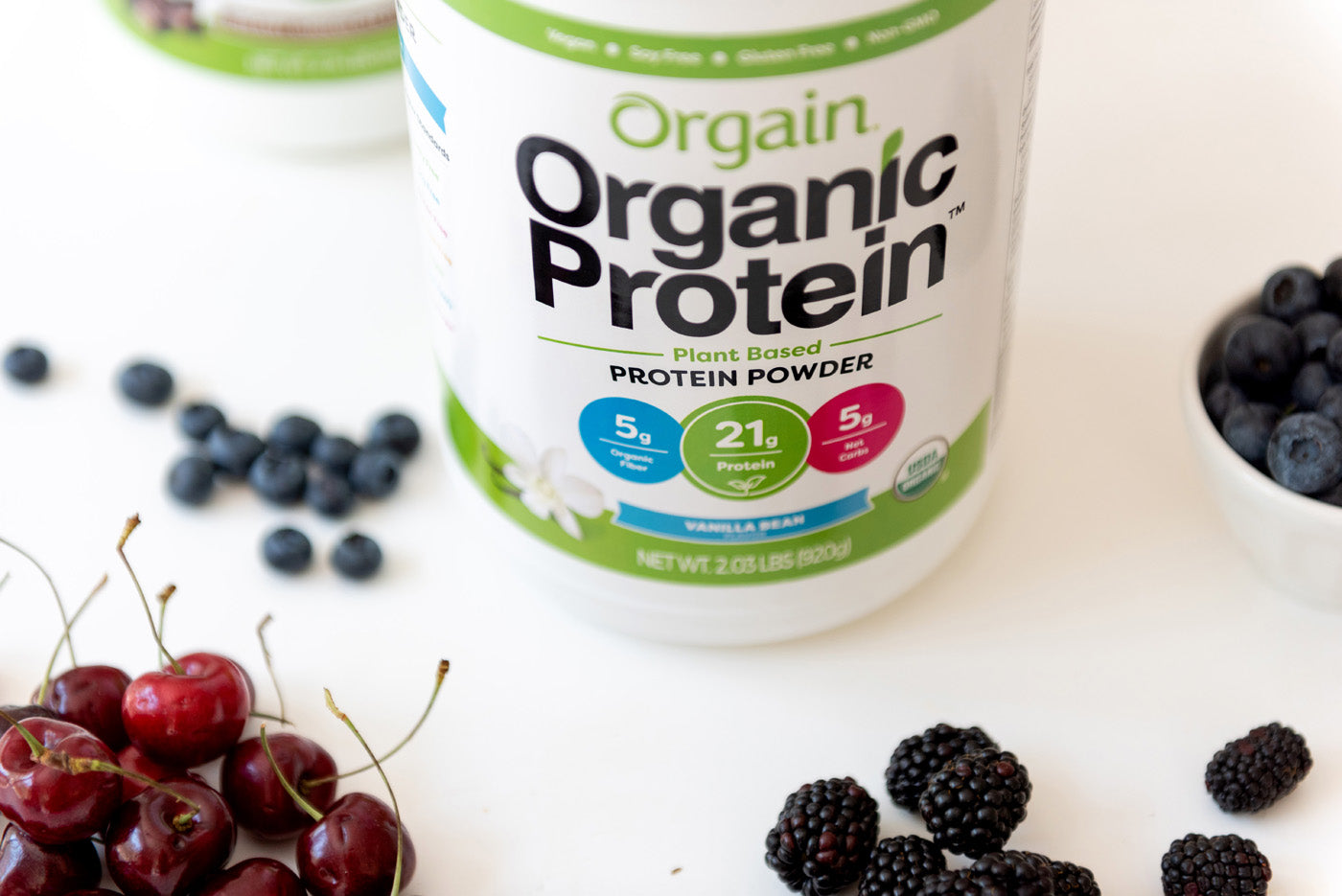 A canister of Orgain Organic Protein powder sitting next to some fresh fruit