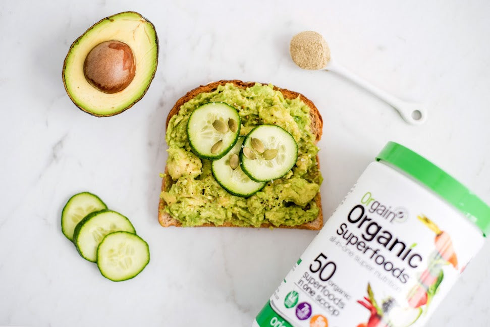 A slice of avocado toast sitting next to a canister of Orgain's Organic Superfoods