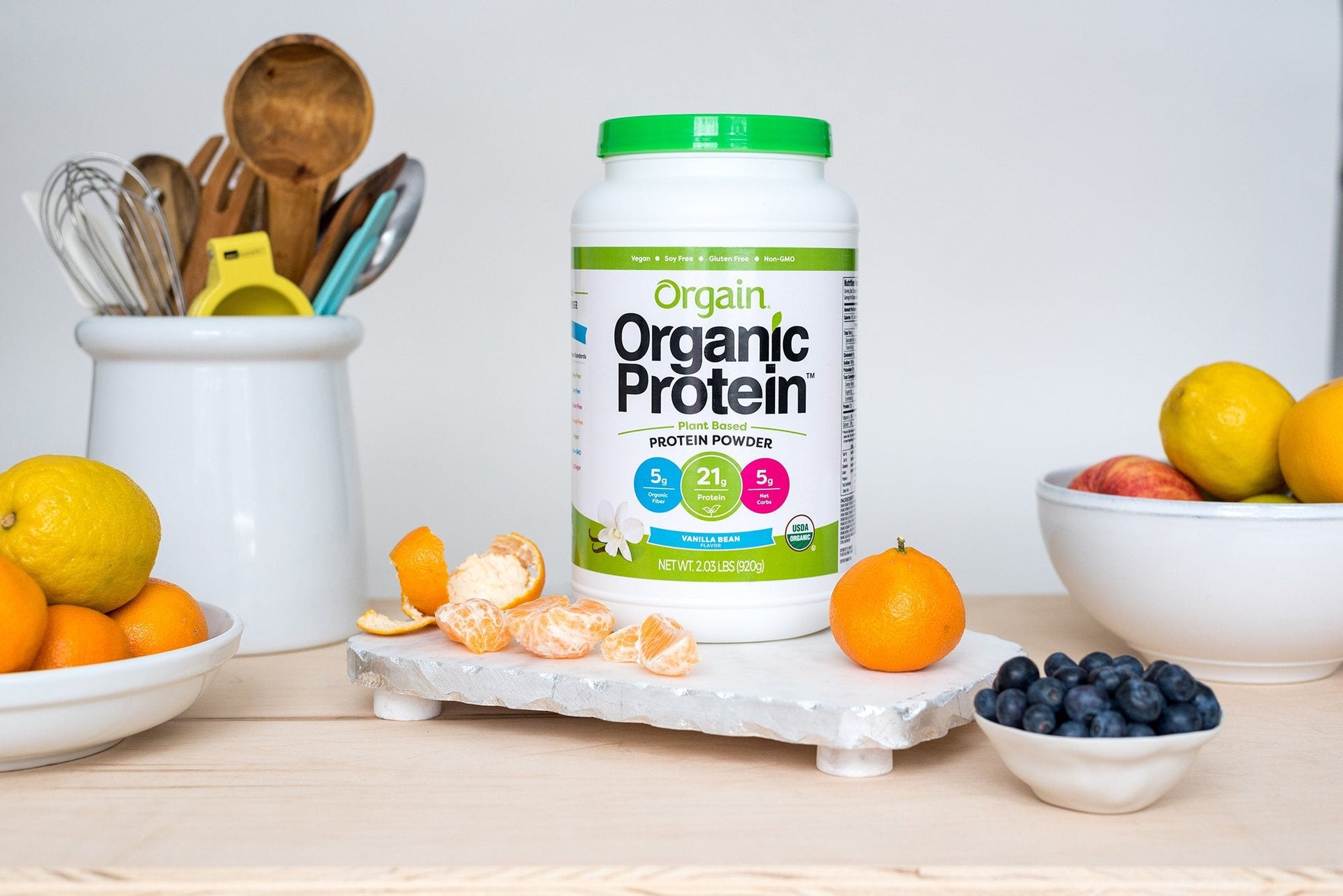 Orgain's Organic Protein powder sitting next to fresh fruit on a kitchen counter