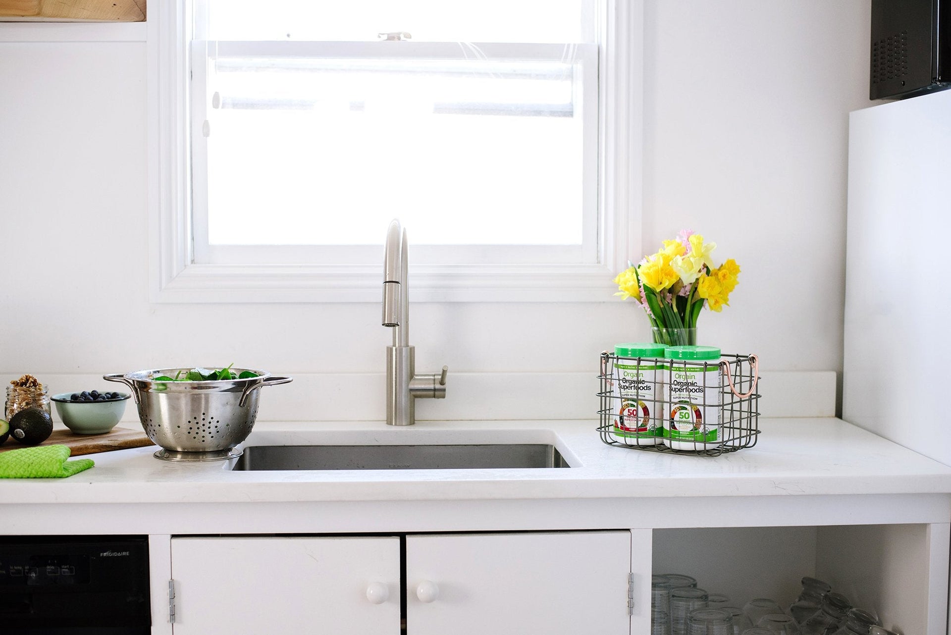 A basket of Orgain products sitting on the counter beside the sink in a ktichen.