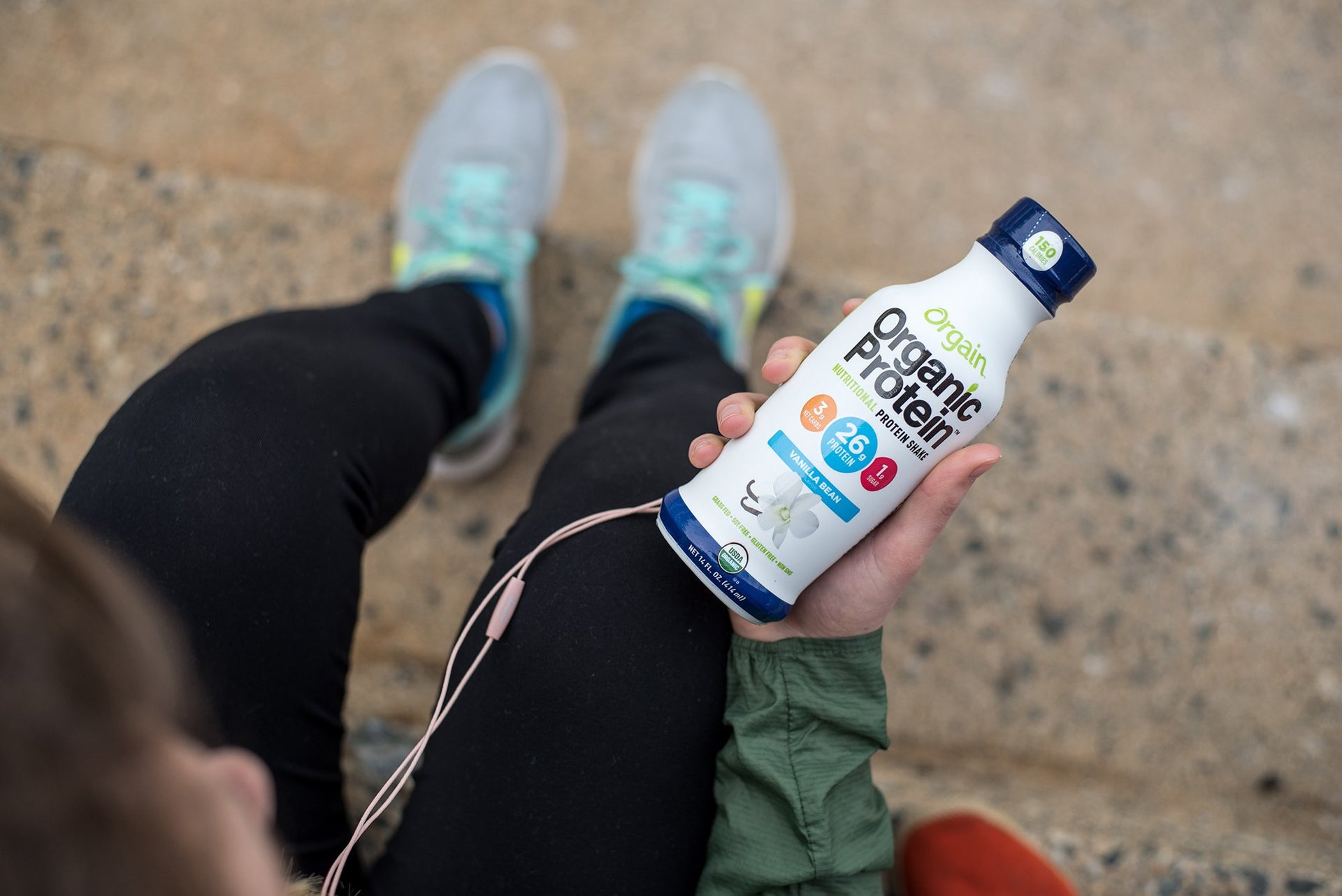 A female athlete takes a break from her run to hold up her Organic Protein shake by Orgain.