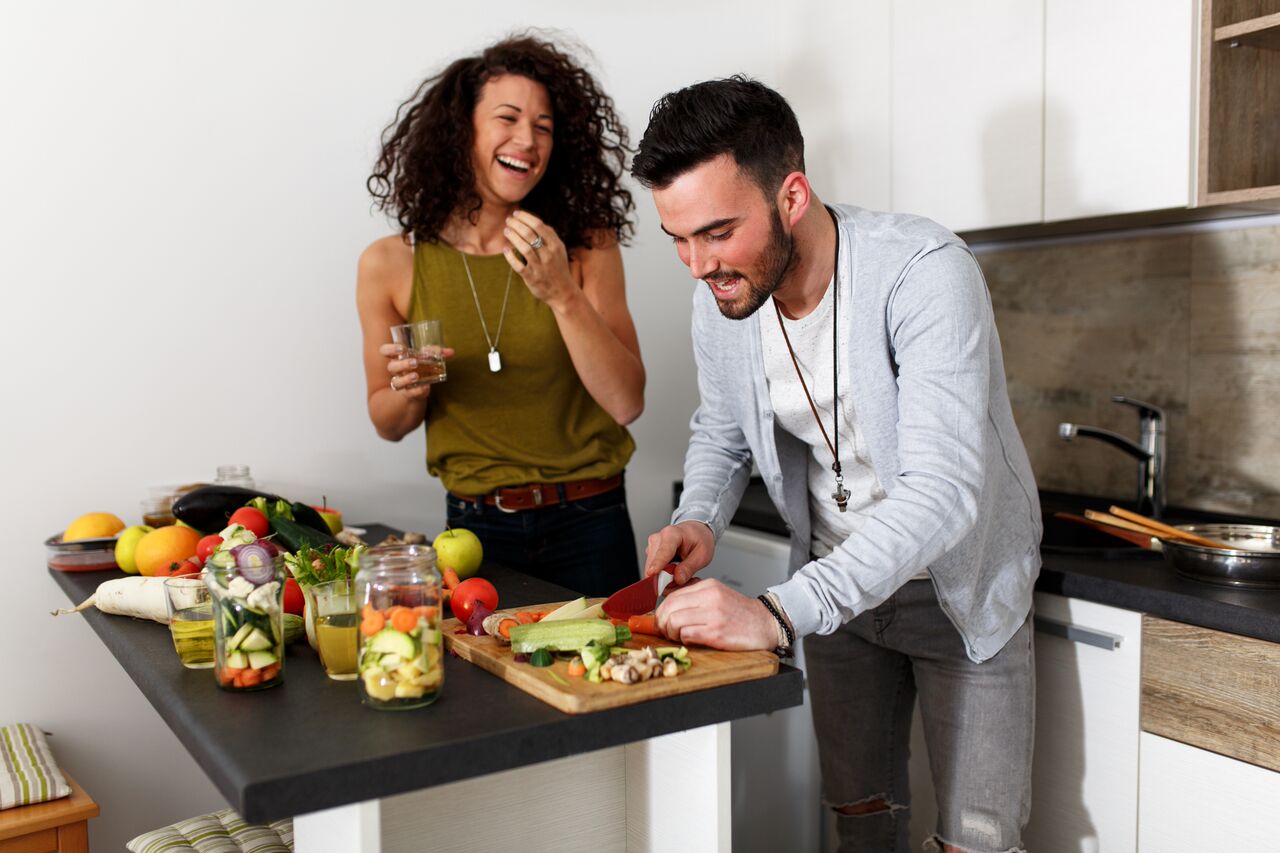 A happy couple prepares ah healthy, veggie-filled dinner in the kitchen.