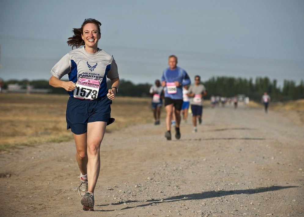 A smiling female athlete leads the other race contestants down a flat, gravel road.