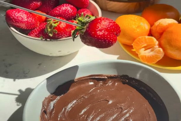 Bowl of rich chocolate fondue surrounded by fresh strawberries and mandarin oranges ready for dipping