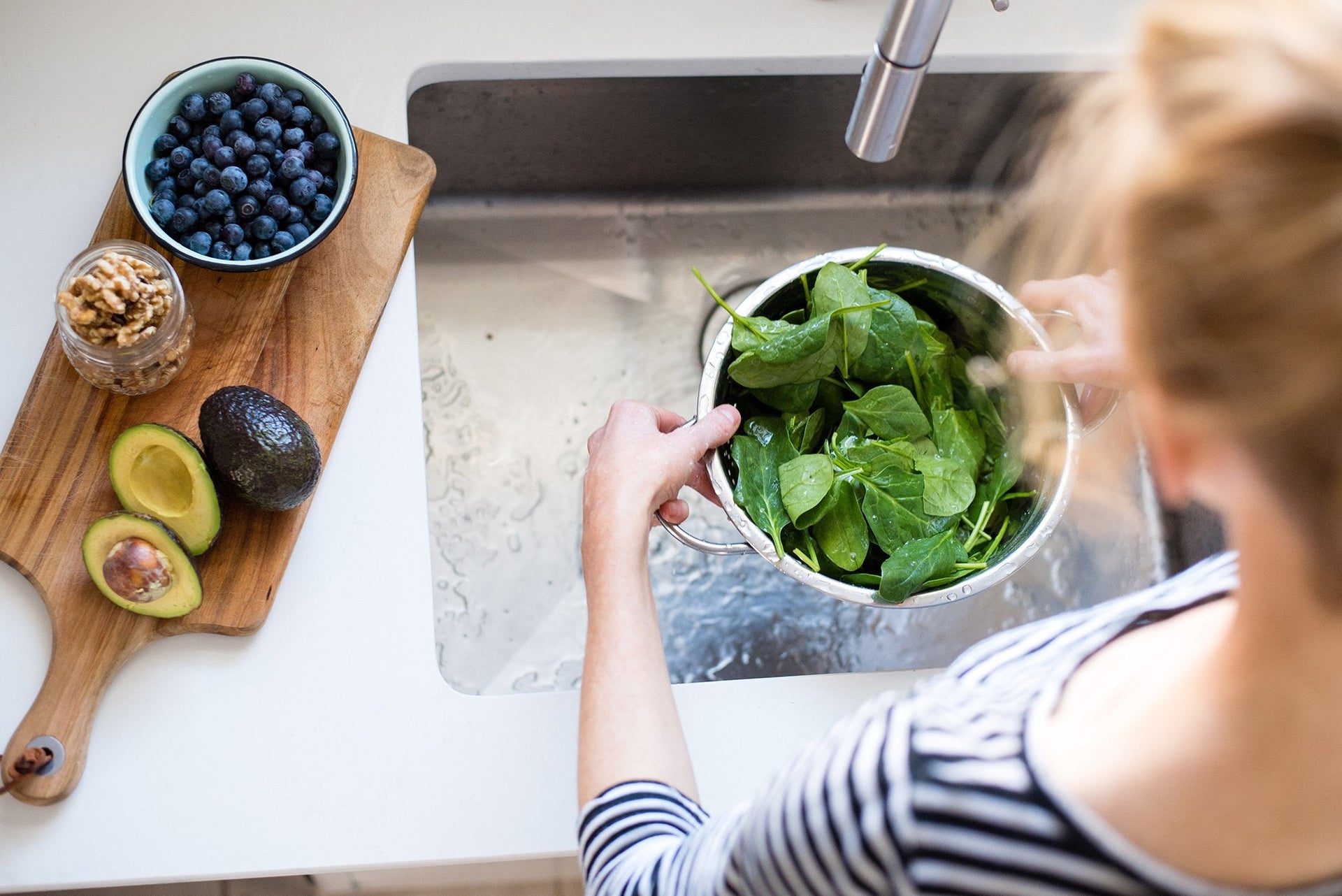 A woman washing greens in the kitchen sink in preparation for a recipe.