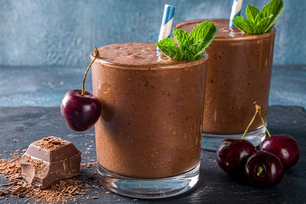 Chocolate cherry protein smoothie made with Orgain chocolate protein powder, topped with fresh mint and surrounded by cherries and chocolate.
