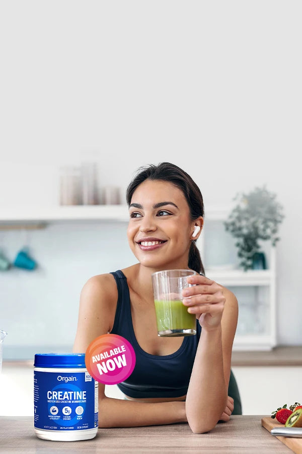 woman drinking a green beverage with Orgain creatine on kitchen counter