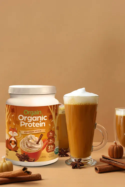 Orgain Organic Protein Pumpkin Spice flavor container with a pumpkin spice latte on a brown background